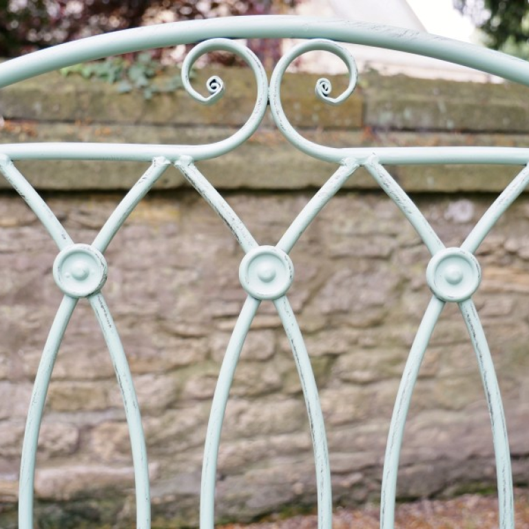 Decorative metal bench with intricate designs against a stone wall background