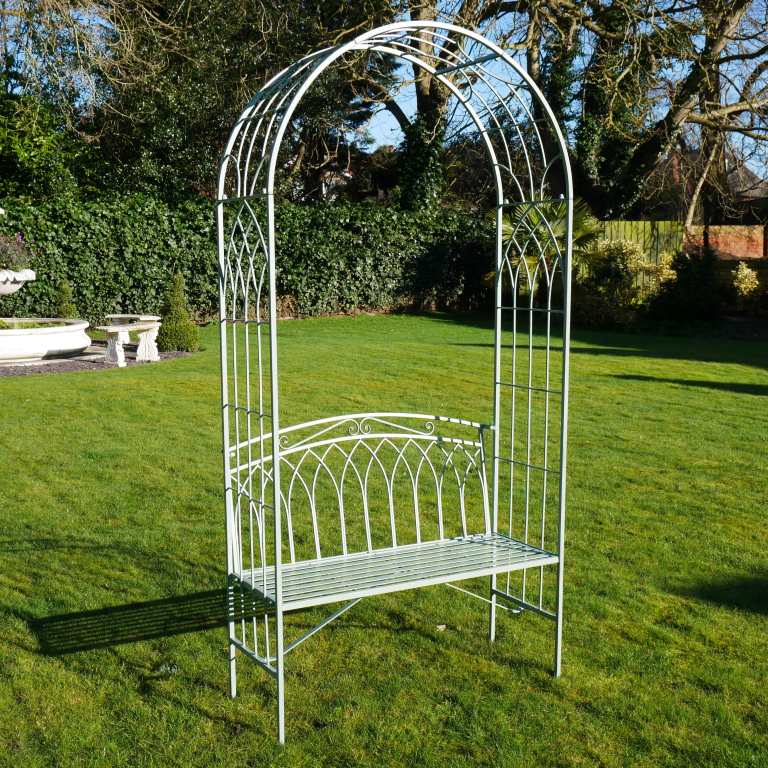 Metal garden arch with bench on a grassy lawn with a fountain in the background