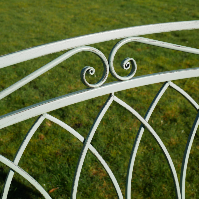 Decorative metal bench armrest with intricate scrollwork on a grassy background