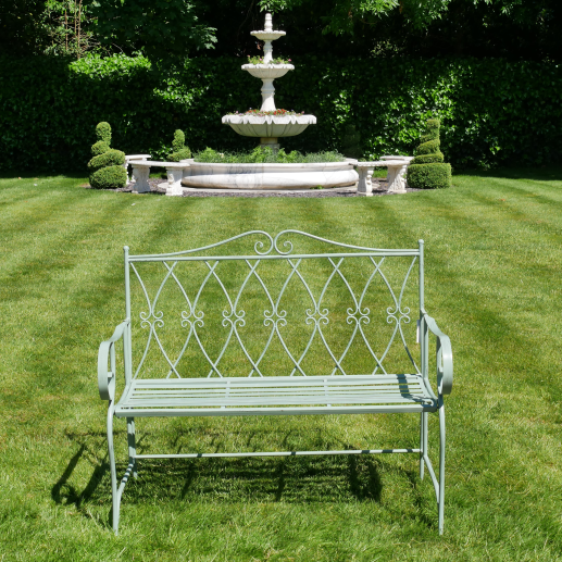 Wrought iron bench on a grassy lawn with a fountain in the background