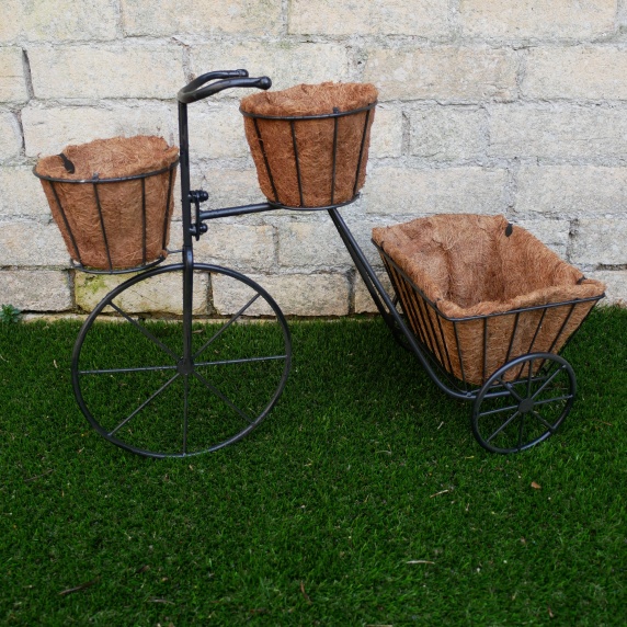 Decorative metal bike with three woven basket planters against a stone wall.