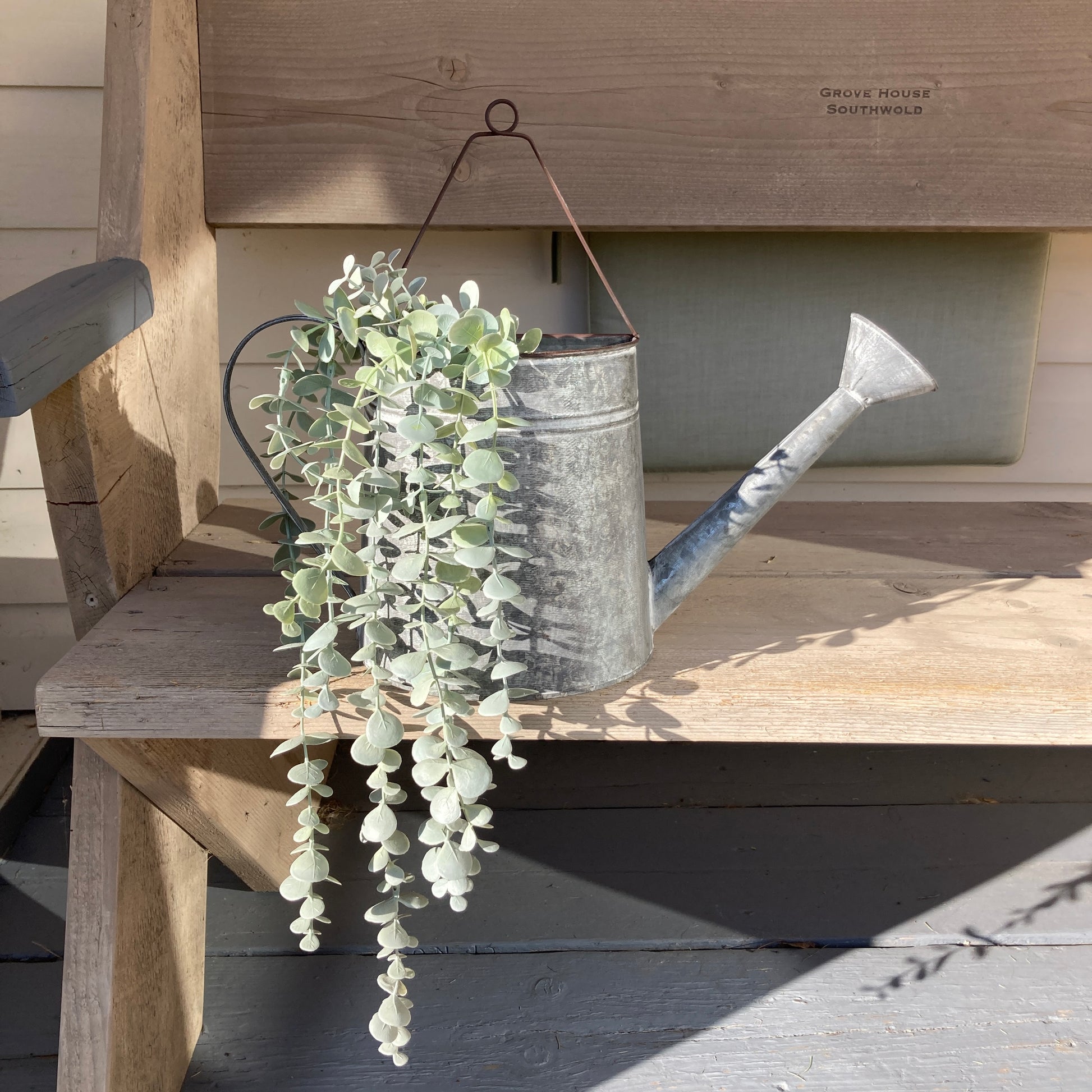 Zinc wall hanging watering can planter - on bench. 