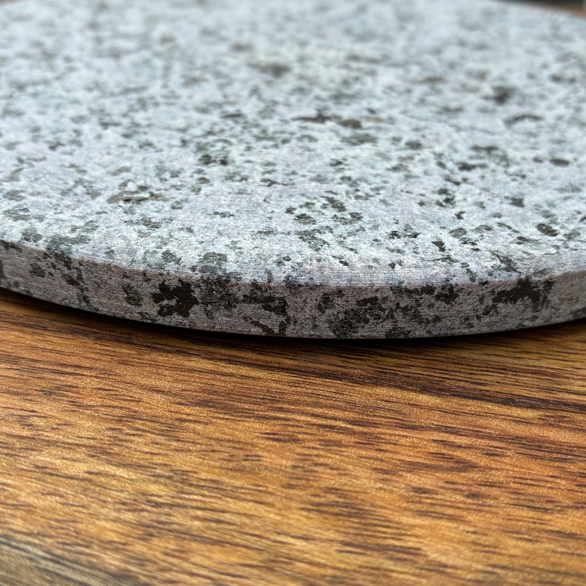 Close-up of a gray speckled GRANITE TRIVET on a wooden surface