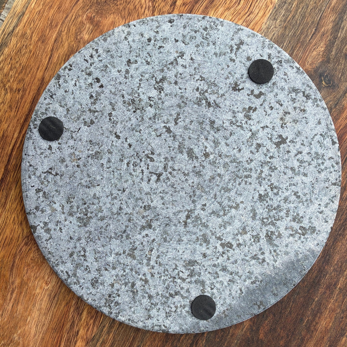 Round granite trivet underside with three black circular pads on a wooden surface