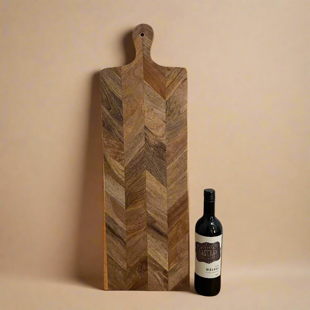 Wooden cutting board with a chevron pattern next to a bottle of wine on a beige background