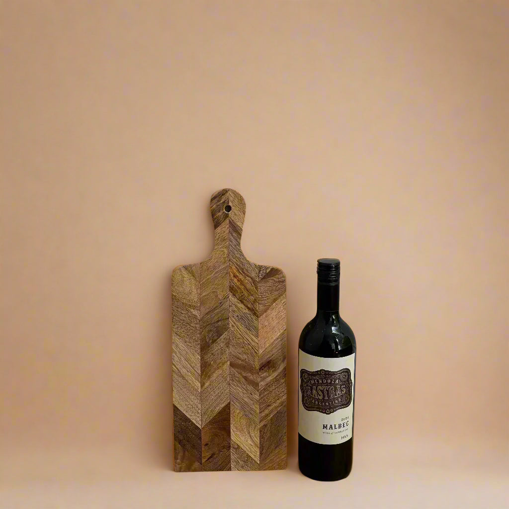 Wooden cutting board with a bottle of wine on a wooden floor against a white wall.