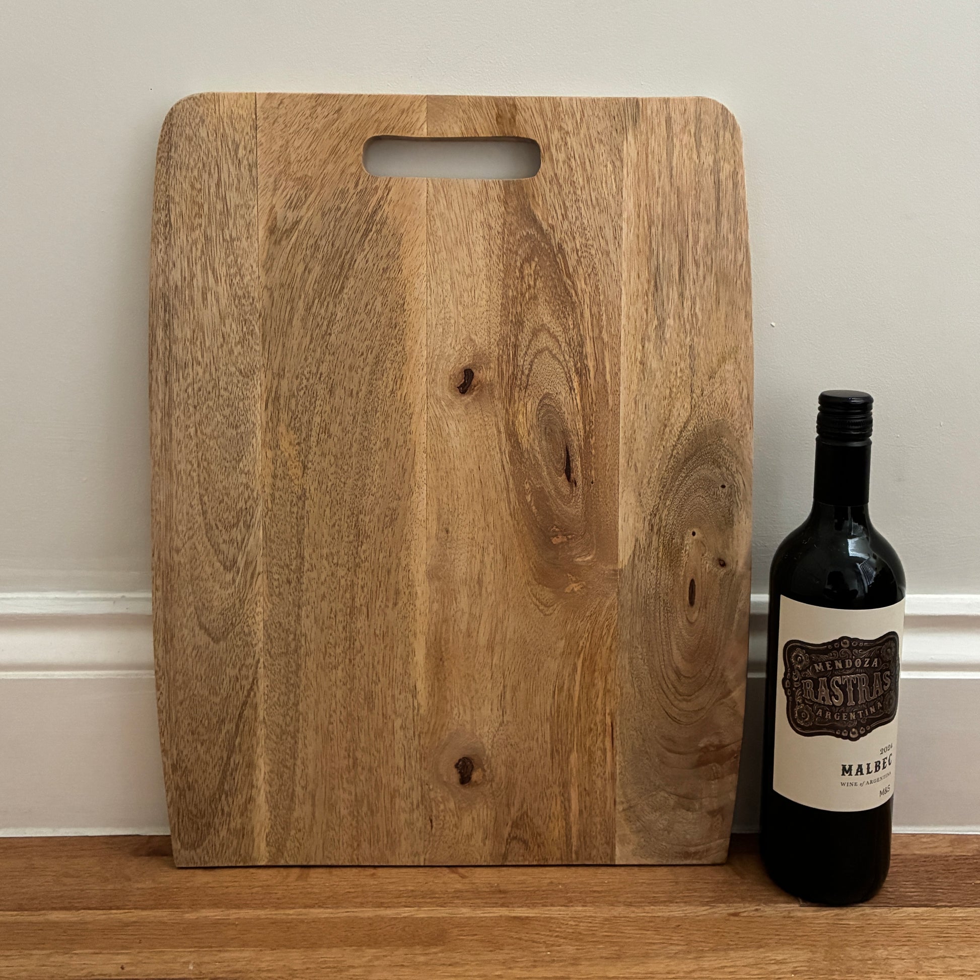 Wooden cutting board with a bottle of wine on a wooden surface.