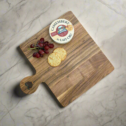 Wooden cutting board with Camembert cheese, grapes, and crackers on a grey wooden floor.