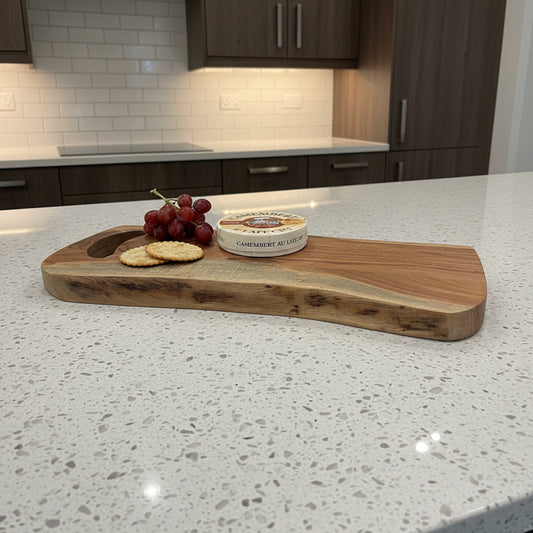Wooden cutting board with cheese, crackers, and grapes on a gray wooden floor.
