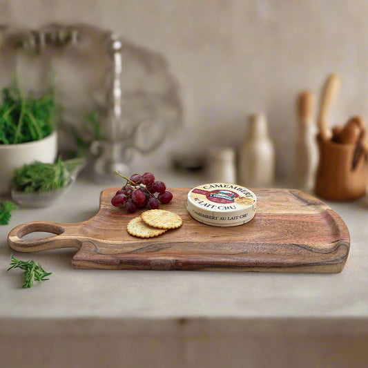 Wooden cutting board with Camembert cheese, grapes, and crackers on a wooden floor.