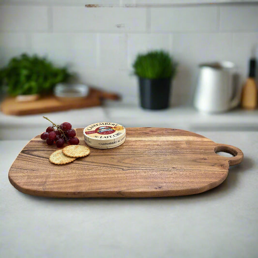 Wooden cutting board with grapes, crackers, and a round cheese on a kitchen counter.