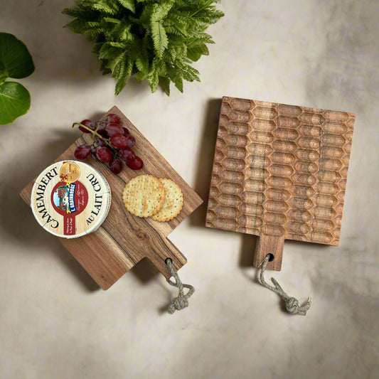 Two wooden cutting boards with a cheese wheel, crackers, and grapes on a grey wooden surface.