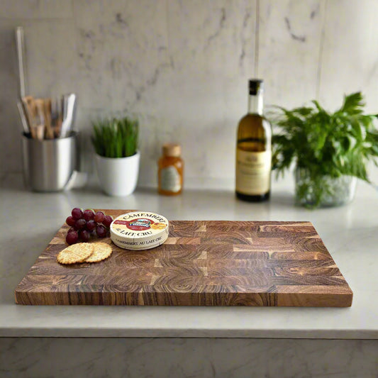 Wooden cutting board with a block of cheese, crackers, and grapes on a gray background