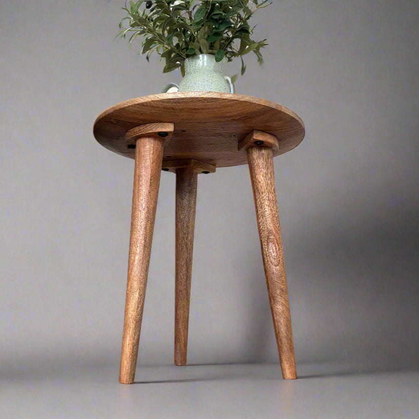 Wooden stool with three legs on a wooden floor in a room.