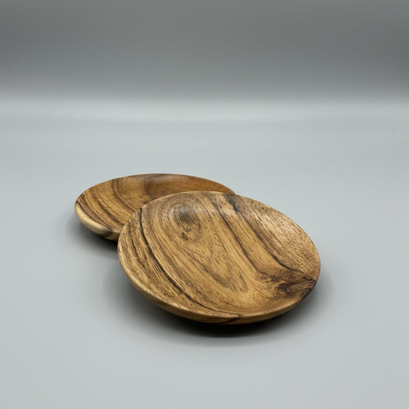 Two wooden coasters on a gray surface with a brown cardboard box in the background.