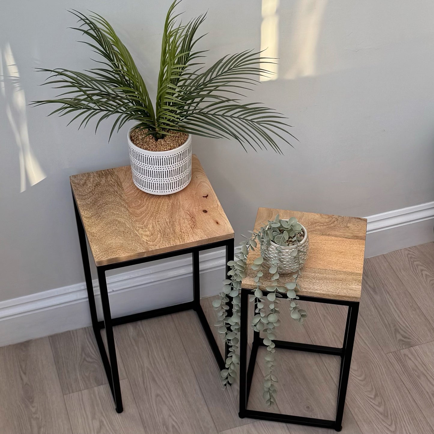 Two small wooden tables with plants on a light wood floor against a gray wall.