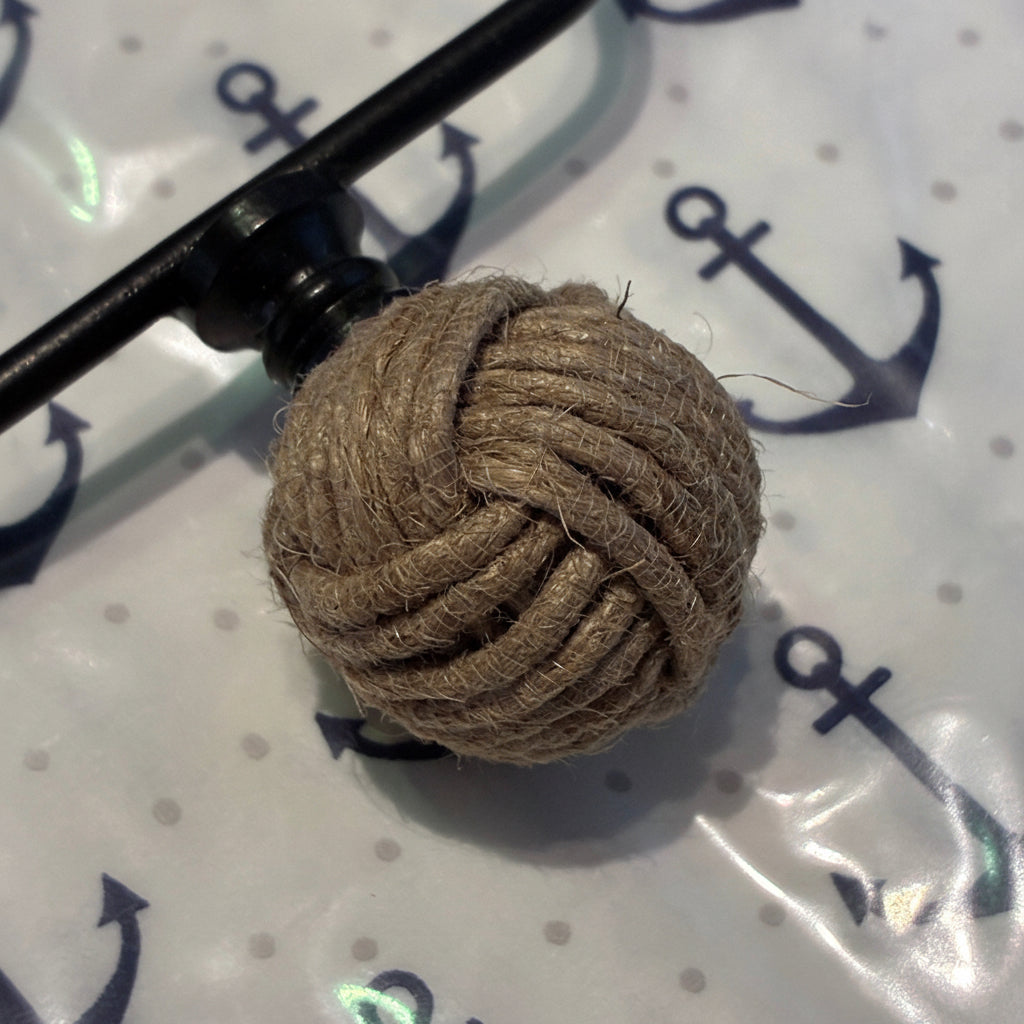 Ball of brown rope tied in a knot on a black metal hook against a white background with anchor patterns.