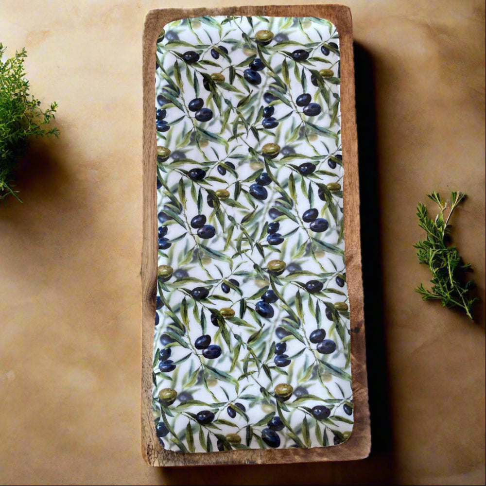 Rectangular tray with olive pattern on a wooden block, surrounded by greenery on a beige background