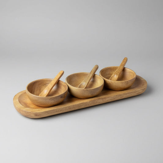 Set of three wooden bowls with spoons on a wooden tray on a table.