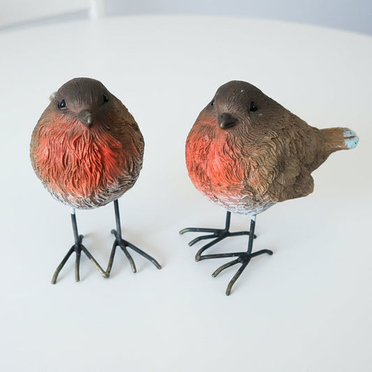 Two decorative bird figurines on a wooden floor