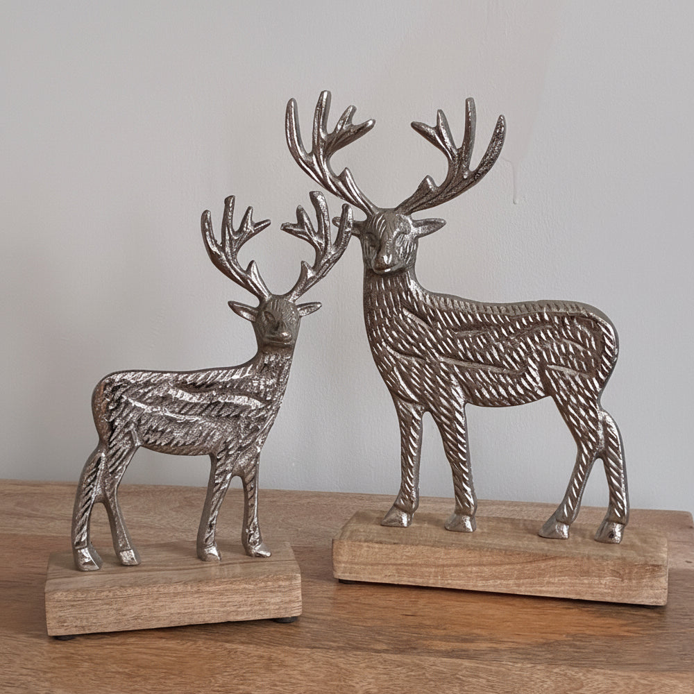 Two metallic deer figurines on wooden bases against a plain background