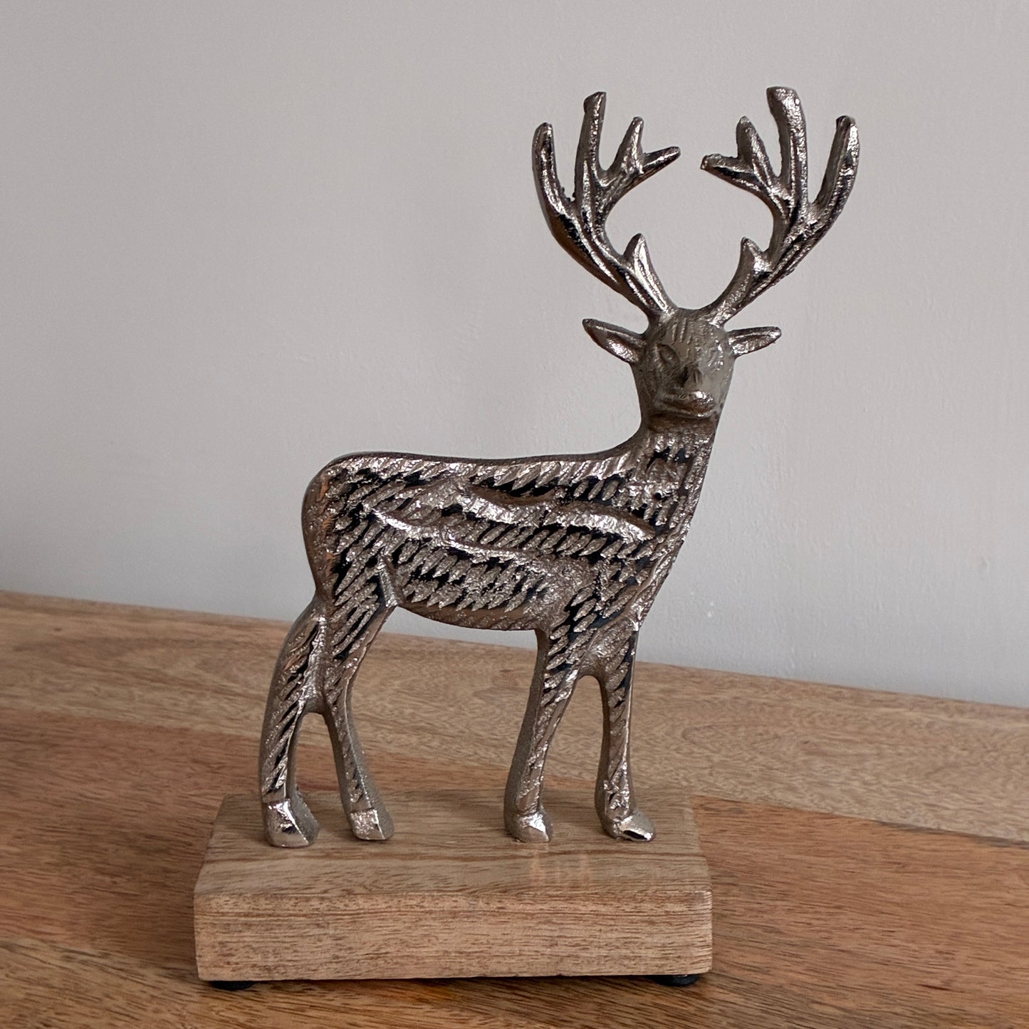 Silver deer figurine on a wooden base against a plain background