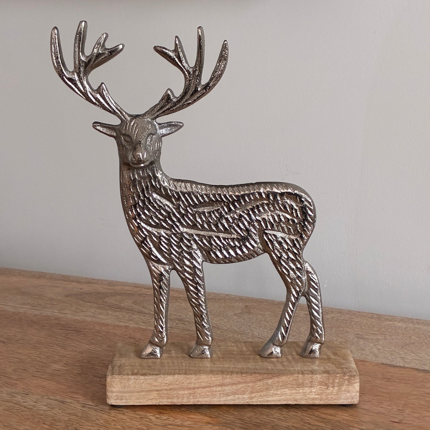 Decorative metal deer figure on a wooden base against a plain background