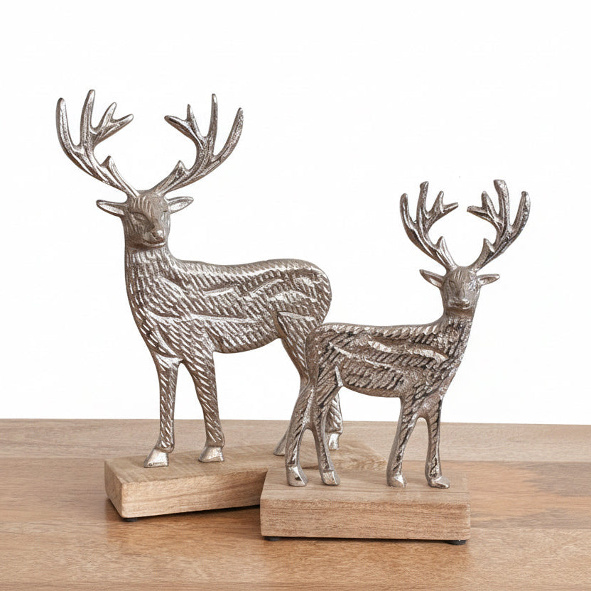Two metallic deer figurines on wooden bases against a plain background