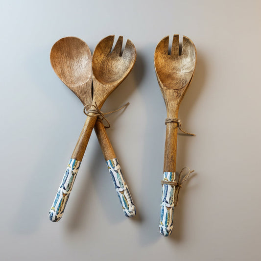Set of wooden salad servers with decorative handles on a wooden surface