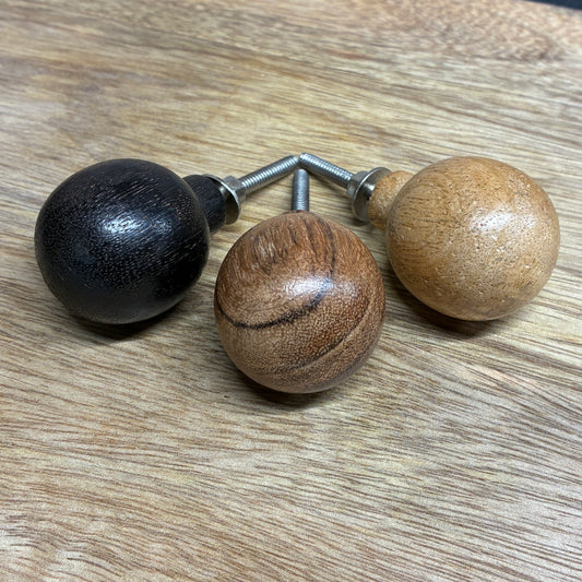 Three wooden knobs in black, brown, and beige on a wooden surface.