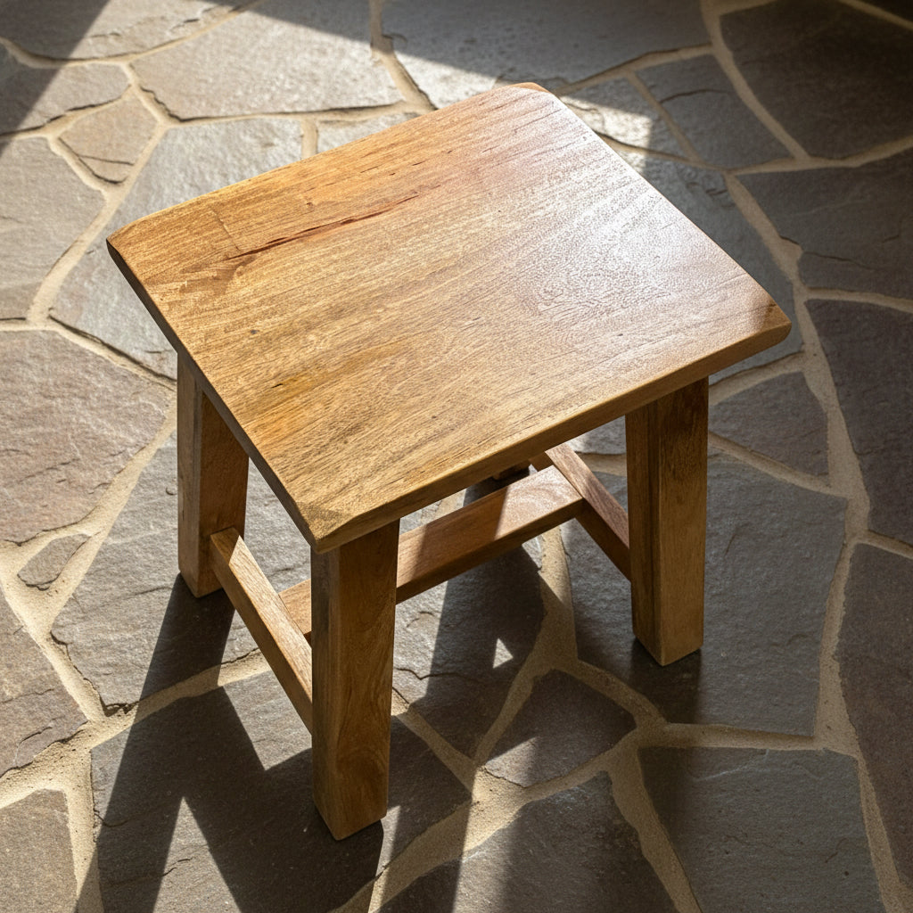 A rustic wooden stool with a square seat and four legs, photographed on a gray concrete floor.