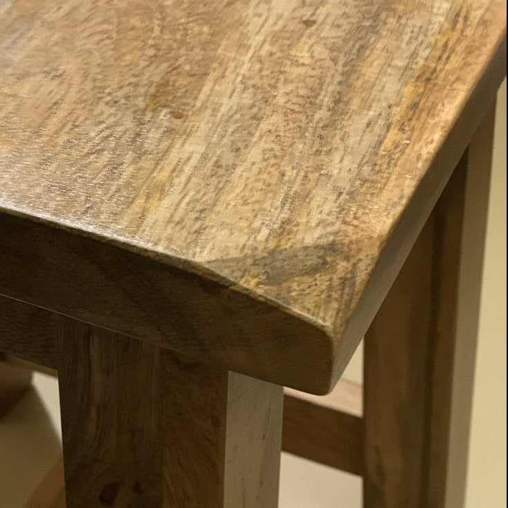 Close-up of a rustic wooden table corner showing the natural grain, polished finish, and thick block legs on a concrete floor.