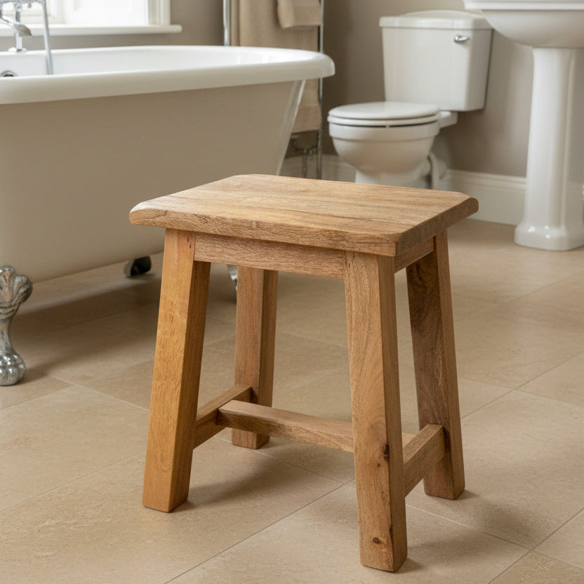 A rustic wooden stool made from natural wood with visible grain, photographed in what appears to be a workshop or warehouse setting on a gray concrete floor.