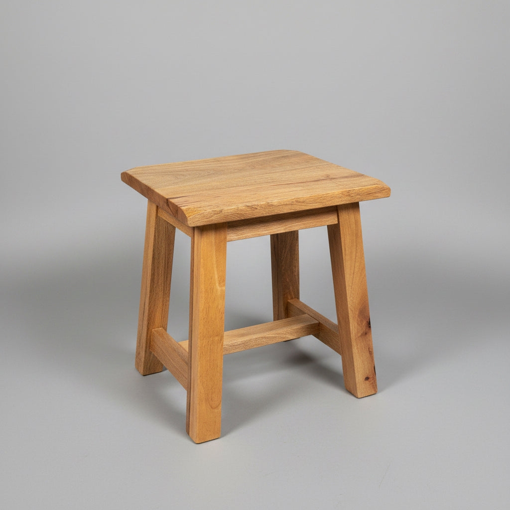 A small wooden stool with a natural light brown wood finish, shown from an angled perspective against a gray concrete or industrial wall background.