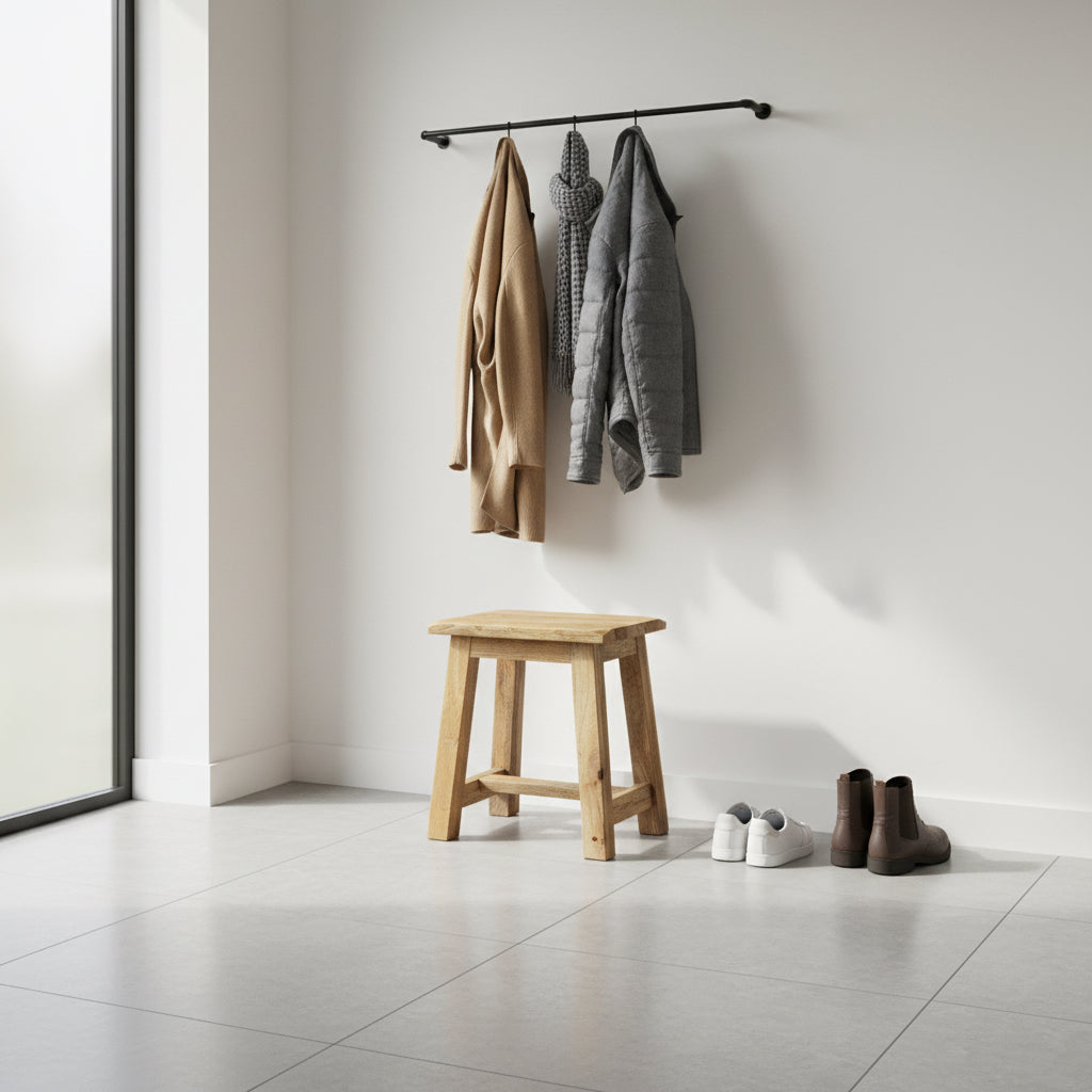 A small square wooden stool with a natural light brown finish, photographed outdoors on a paved surface in front of a weathered wooden fence.