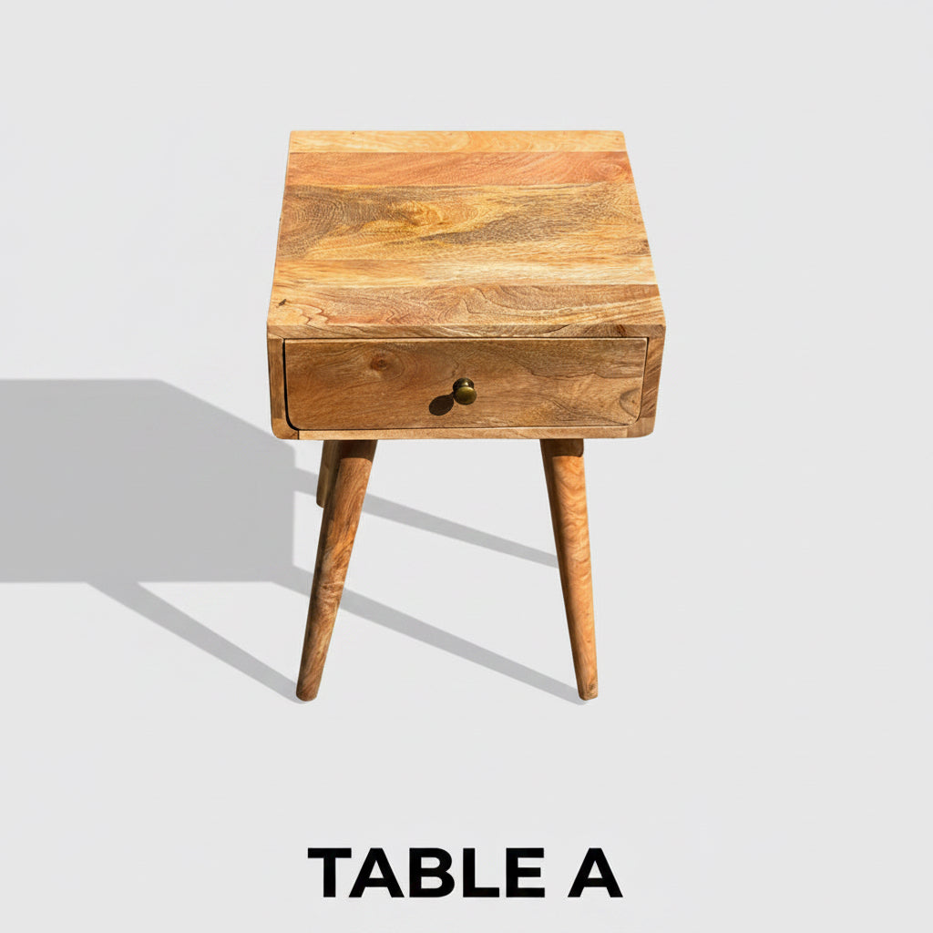 A small wooden side table with a single drawer and tapered legs, photographed outdoors on a concrete surface with a fence and plants in the background.