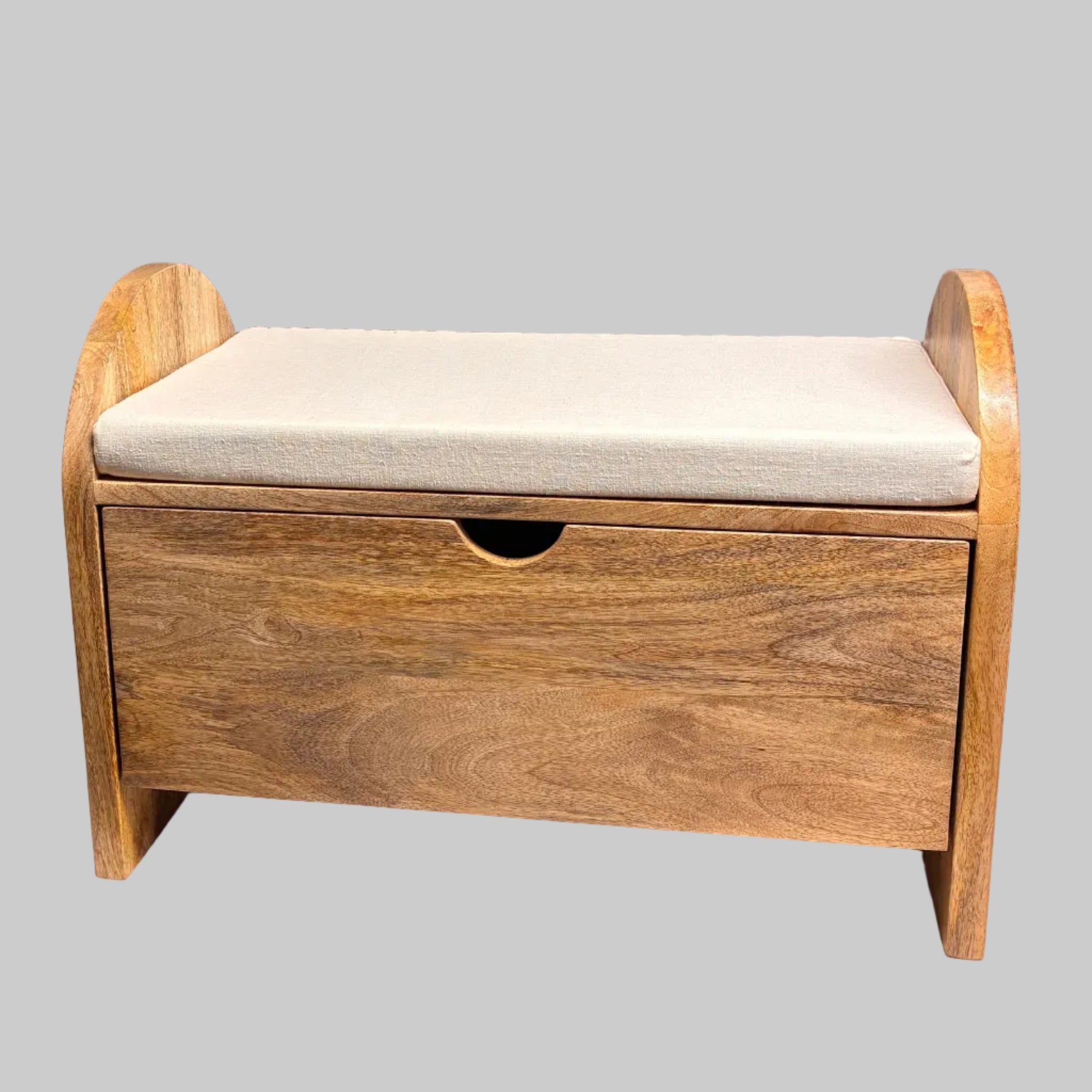 A wooden toy storage bench with a single drawer and a light beige cushioned seat, shown on a white cloth-covered table against a gray wall.