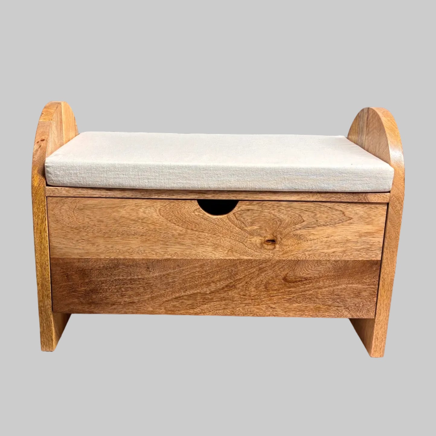 A wooden storage bench with a single drawer and a light beige upholstered seat cushion, placed on a table covered with a white sheet in a workshop setting.
