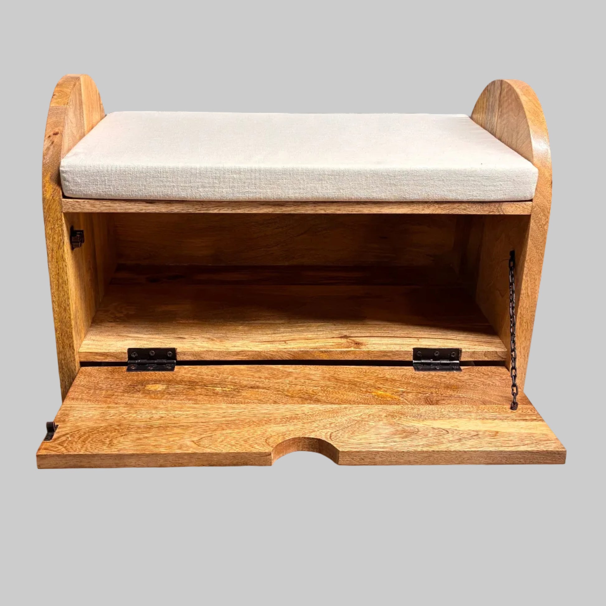 A rustic wooden storage bench with a light beige cushioned seat and an open front compartment, shown on a white-covered table in a workshop or furniture store setting.