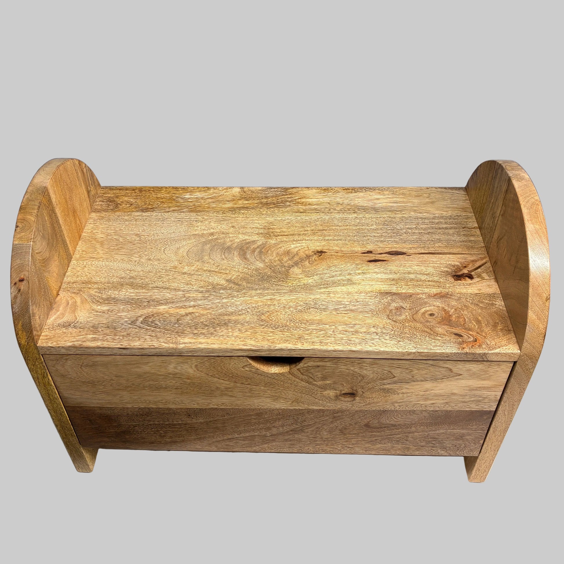 A small wooden storage bench or toy box with a single drawer and curved side supports, shown on a draped white cloth against a plain gray wall.