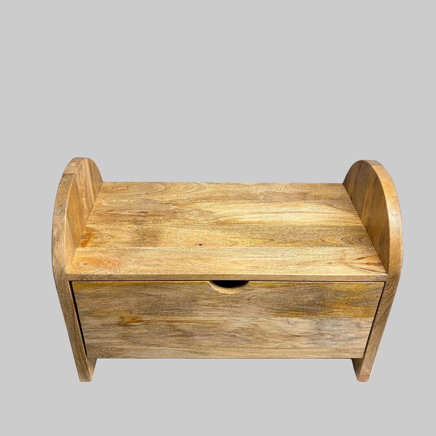 A small wooden storage box or bench with a single drawer and arched sides, shown on a white cloth-covered table against a gray wall.