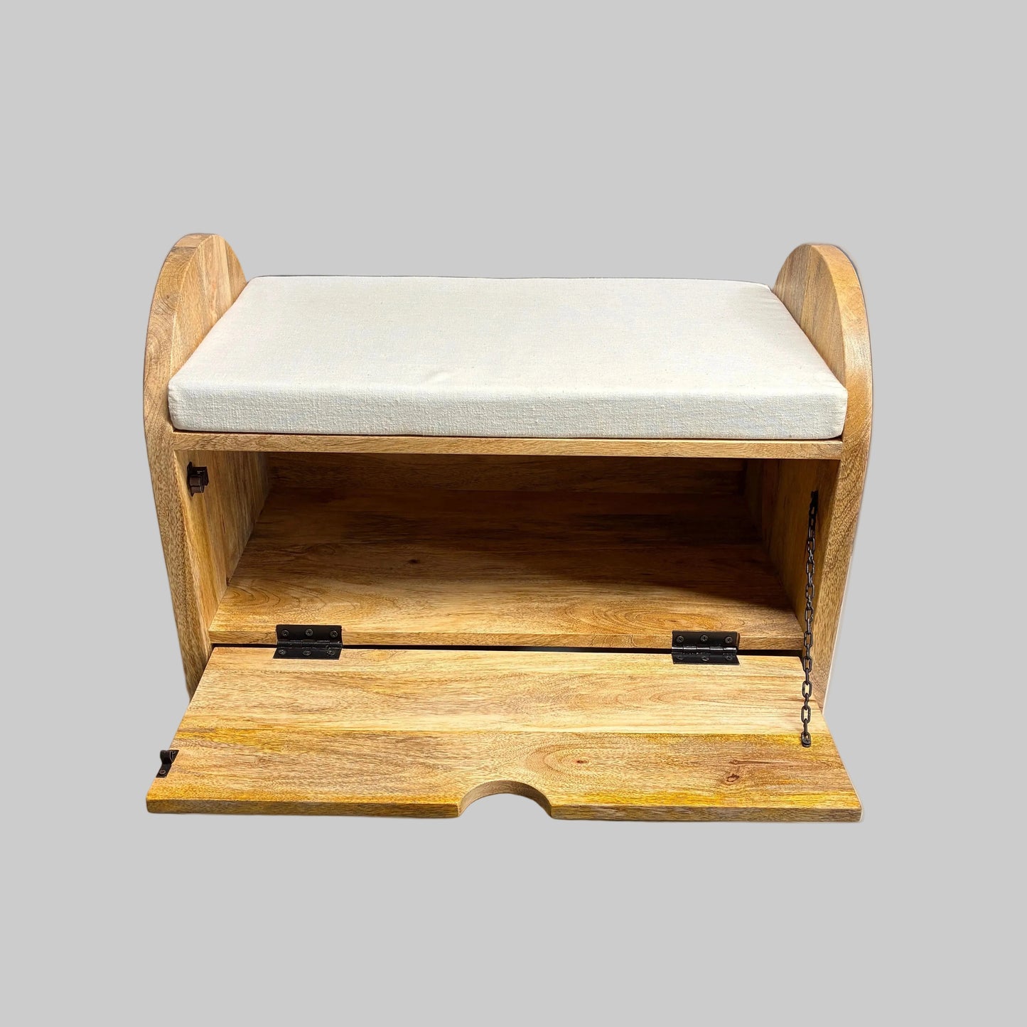 A wooden storage bench with a light beige cushioned seat and an open front door, shown on a draped table in a workshop setting.