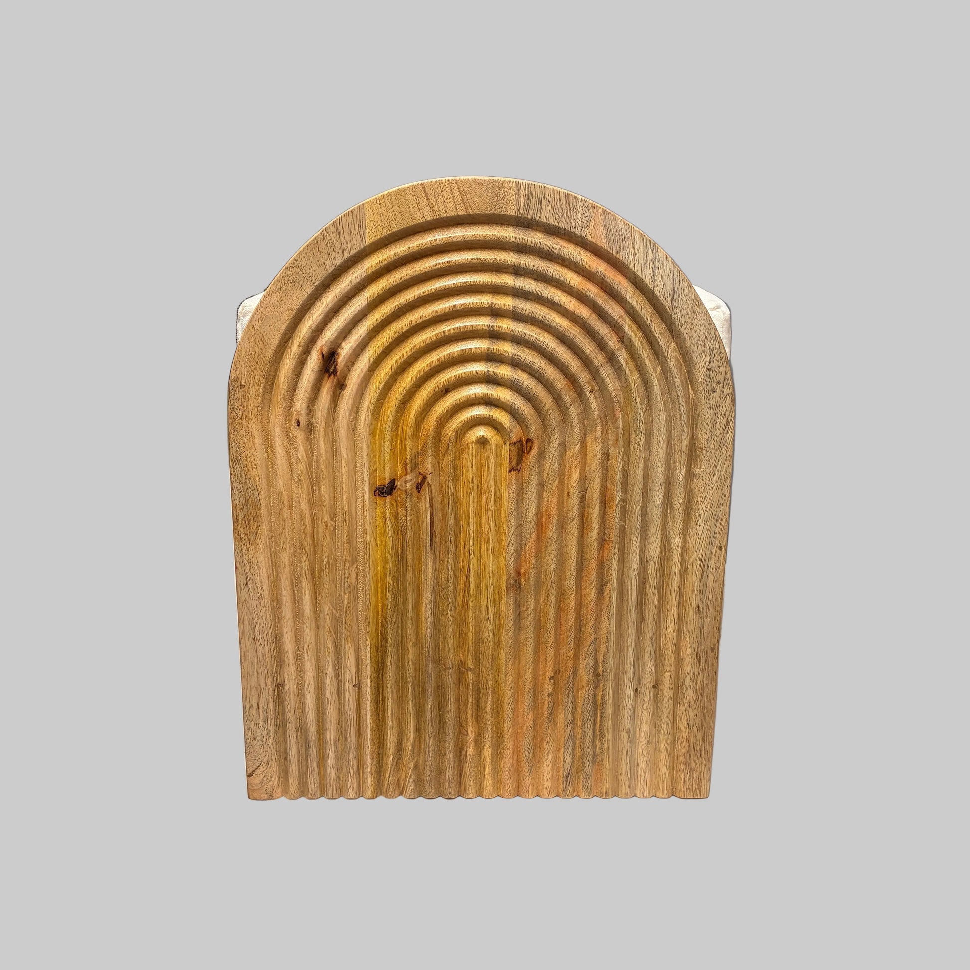 A rectangular wooden board with a rounded top and concentric arched grooves, photographed indoors on a white cloth-covered surface in a workshop or storage area.