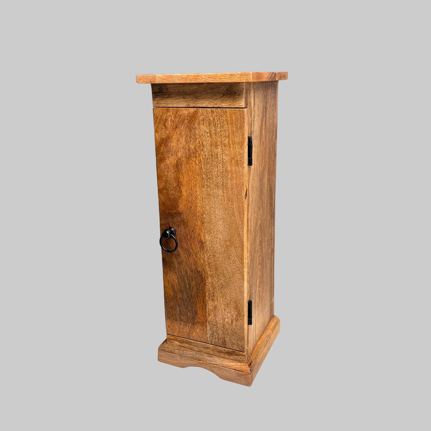 A small rustic wooden cabinet with a single door, black metal hinges, and a round black ring pull handle, shown on a white cloth-covered surface against a gray wall.