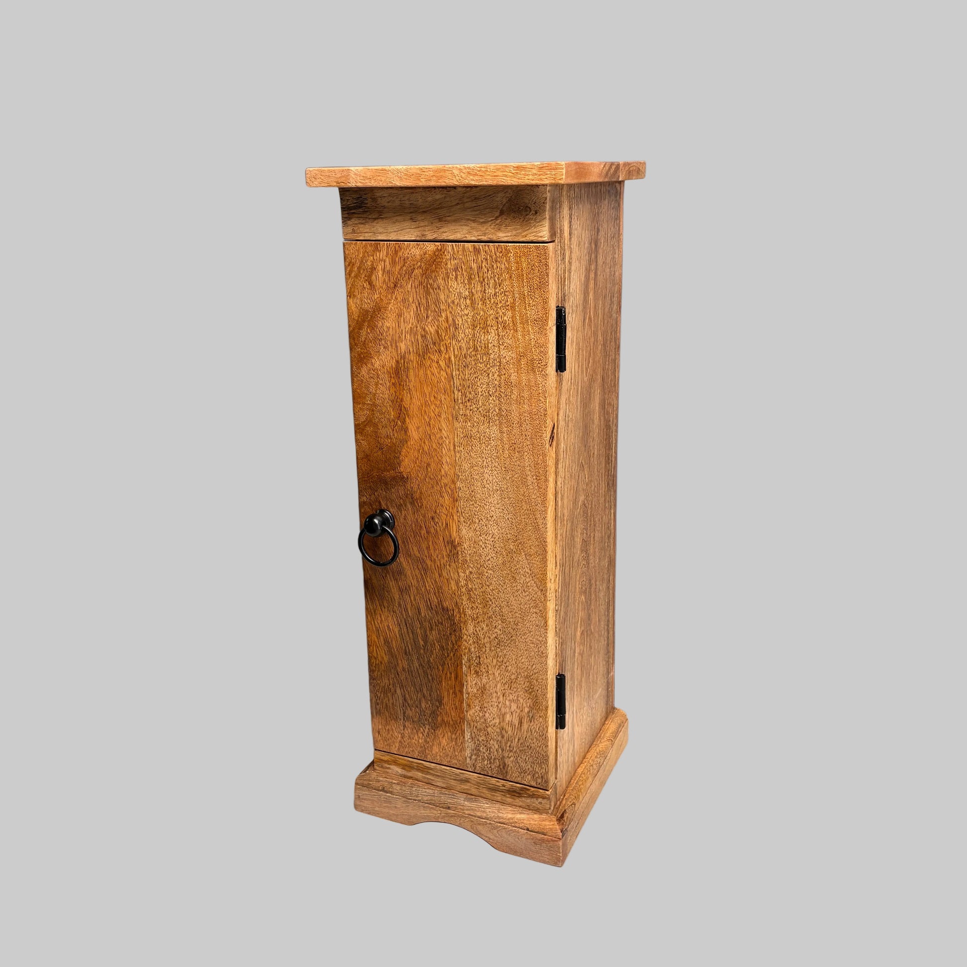 A small rustic wooden cabinet with a single door, black metal hinges, and a round black ring pull handle, shown on a white cloth-covered surface against a gray wall.