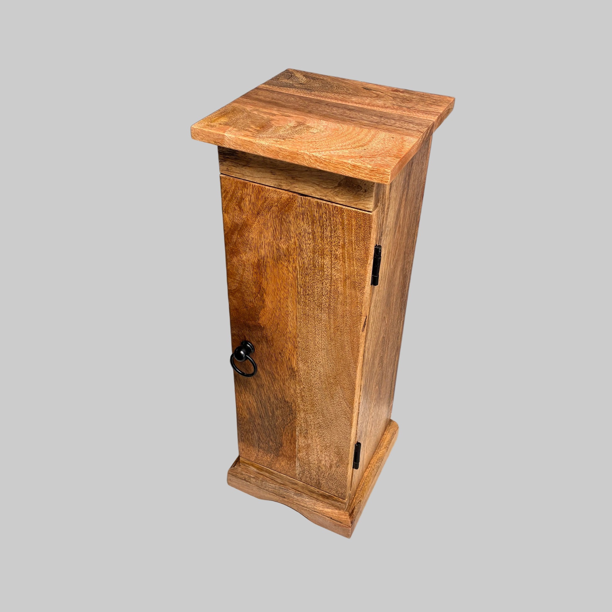 A rustic wooden cabinet with a single door, black metal ring pull, and black hinges, standing on a white fabric-covered surface against a gray backdrop.