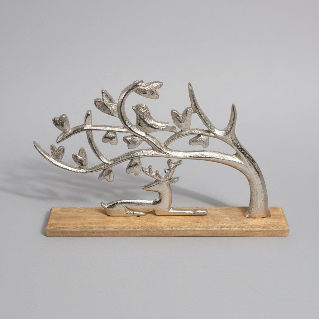 A decorative metal tree sculpture with a deer and birds motif, mounted on a rectangular wooden base against a dark gray wall and light stone surface.