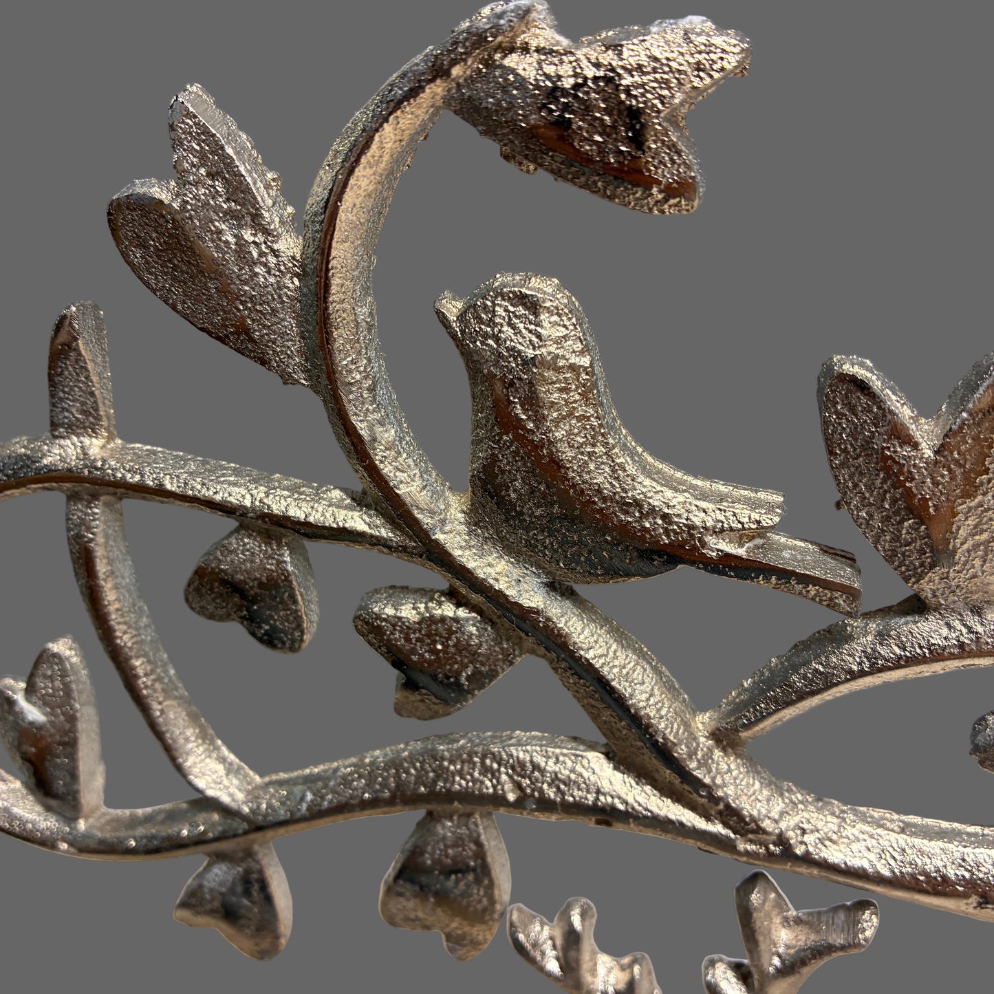 A close-up of a metallic silver bird perched on a branch with textured leaves, shown against a soft gray background.