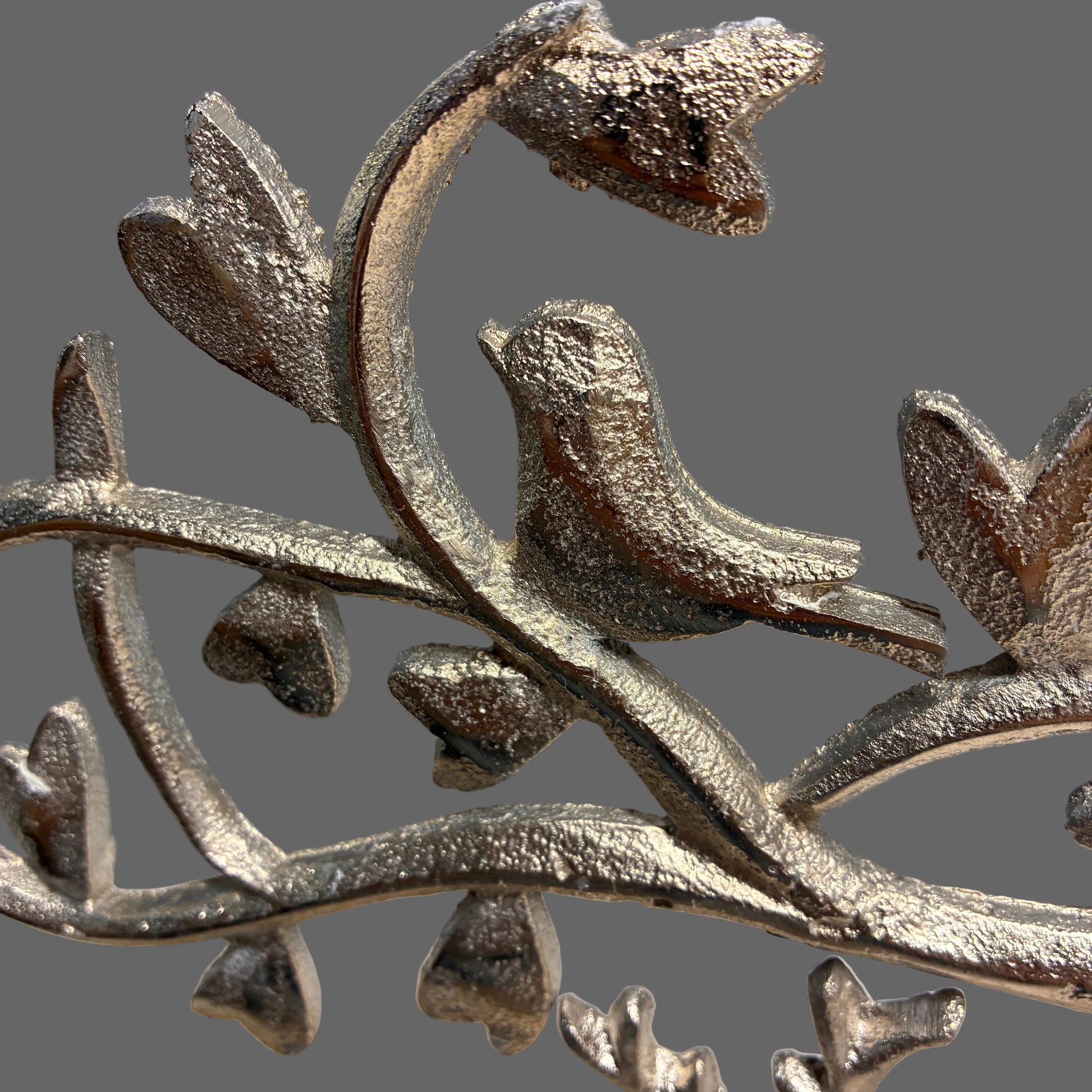 A close-up of a metallic silver bird perched on a branch with textured leaves, shown against a soft gray background.