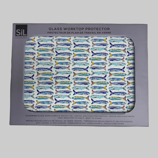 A boxed glass worktop protector with a visible window showing a repeating fish pattern in blue, yellow, and white. The package is placed on a light beige stone-like surface.